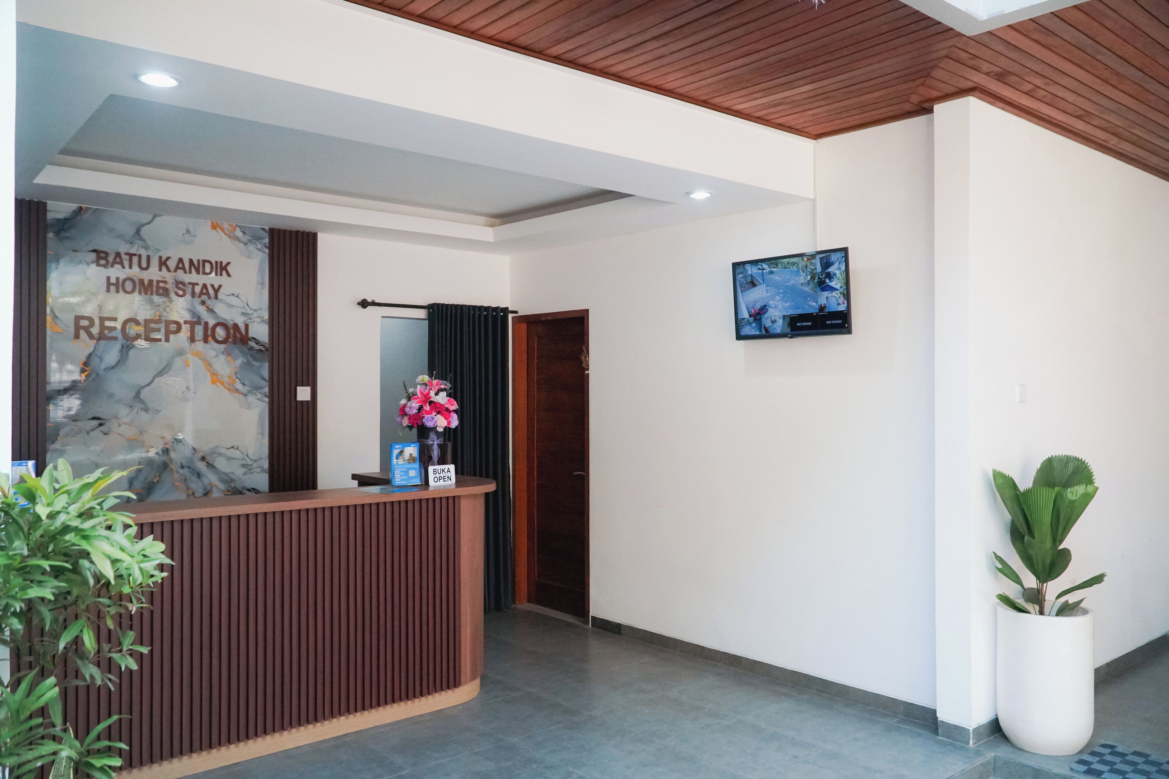 A reception desk with a marble wall, a wooden ceiling, and a flat-screen TV mounted on the wall.