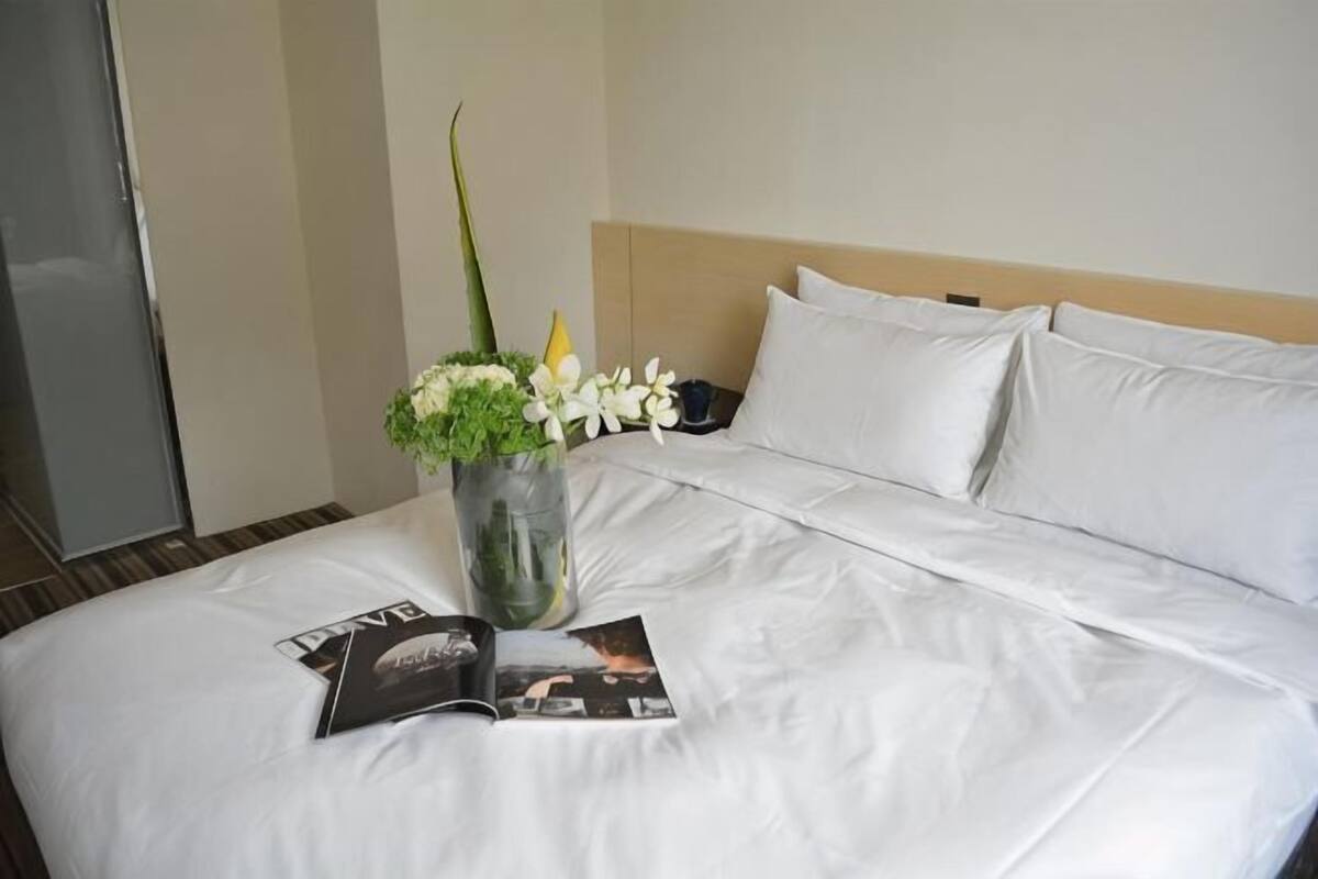 A neatly made bed with white linens, a vase with flowers, and a magazine on the bed.