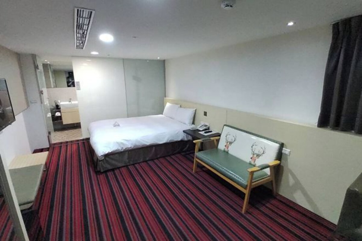 Une chambre d’hôtel avec un lit simple, une table de chevet, une chaise et un petit bureau avec une autre chaise.