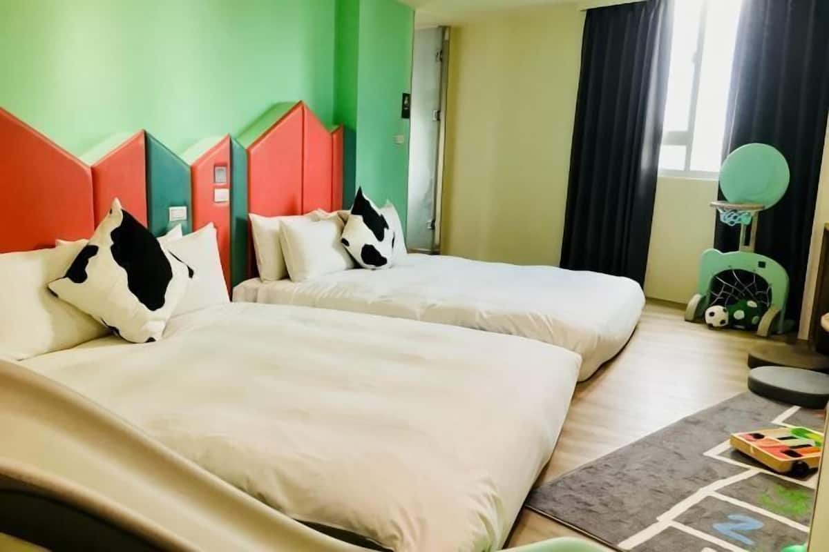 A hotel room with two beds, a green wall, and a window with curtains.