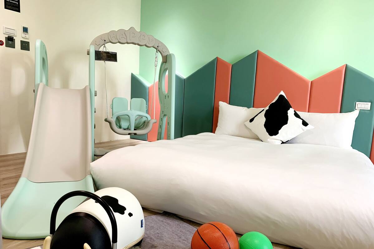 A hotel room with a bed, a child’s play area, and a wall-mounted mirror.