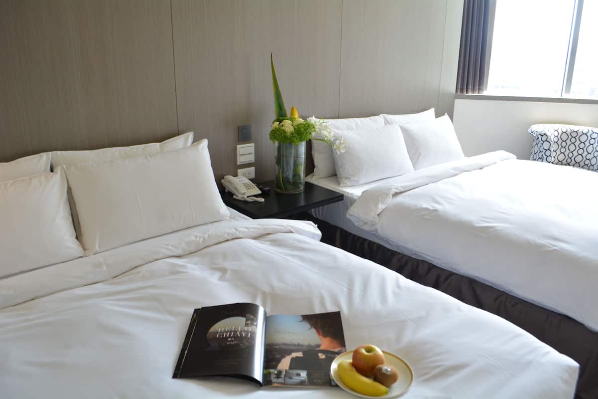 A hotel room with two beds, a bedside table with a phone, a vase with flowers, and a book on the bed.