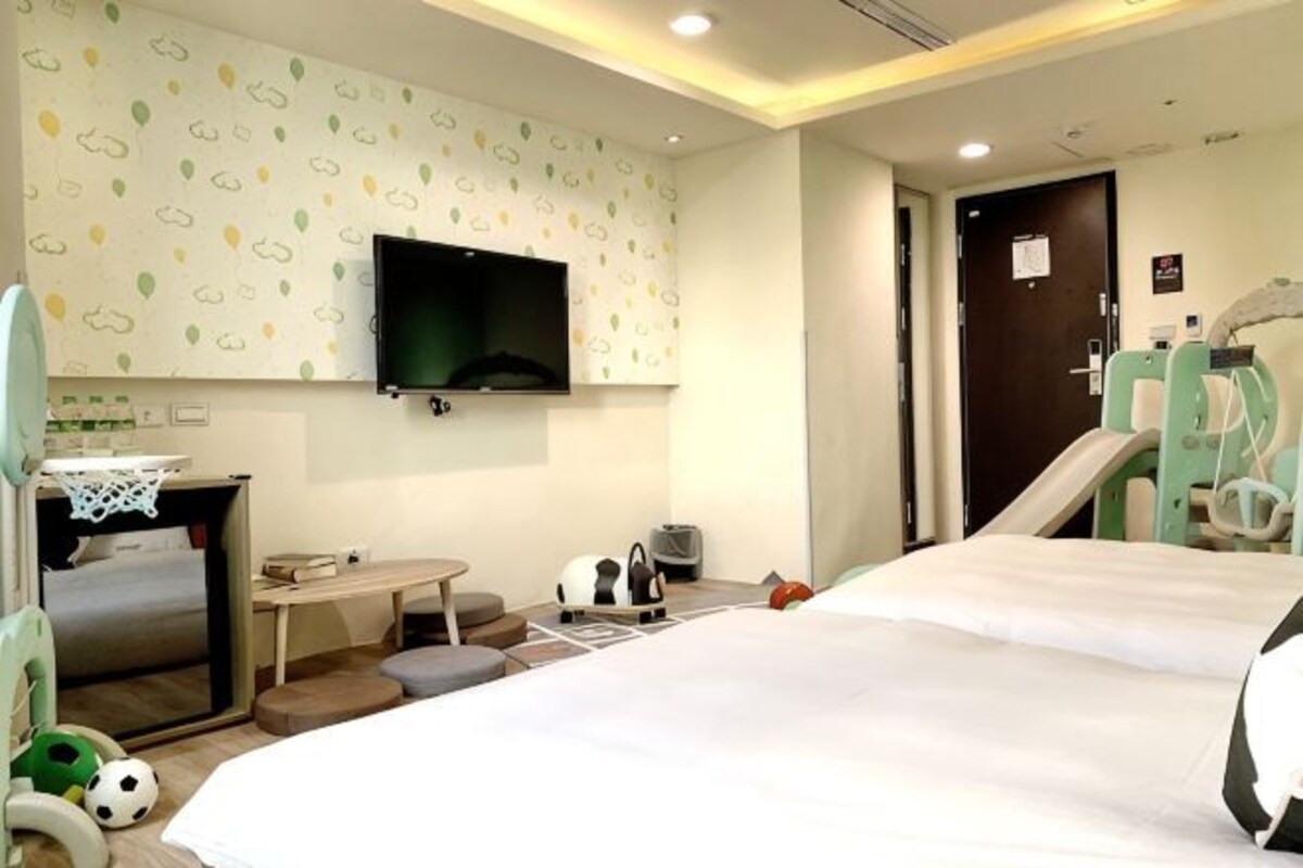 Une chambre d’hôtel avec un lit, un téléviseur fixé au mur, une petite table et un espace de jeux avec des jouets.