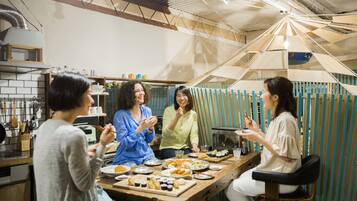 A group of people dining at a wooden table in a rustic kitchen setting with a high ceiling and exposed beams.