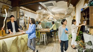 A rustic interior with wooden beams, a long counter, and a group of people interacting. - Guest House MAYA - Hostel (Kobe)
