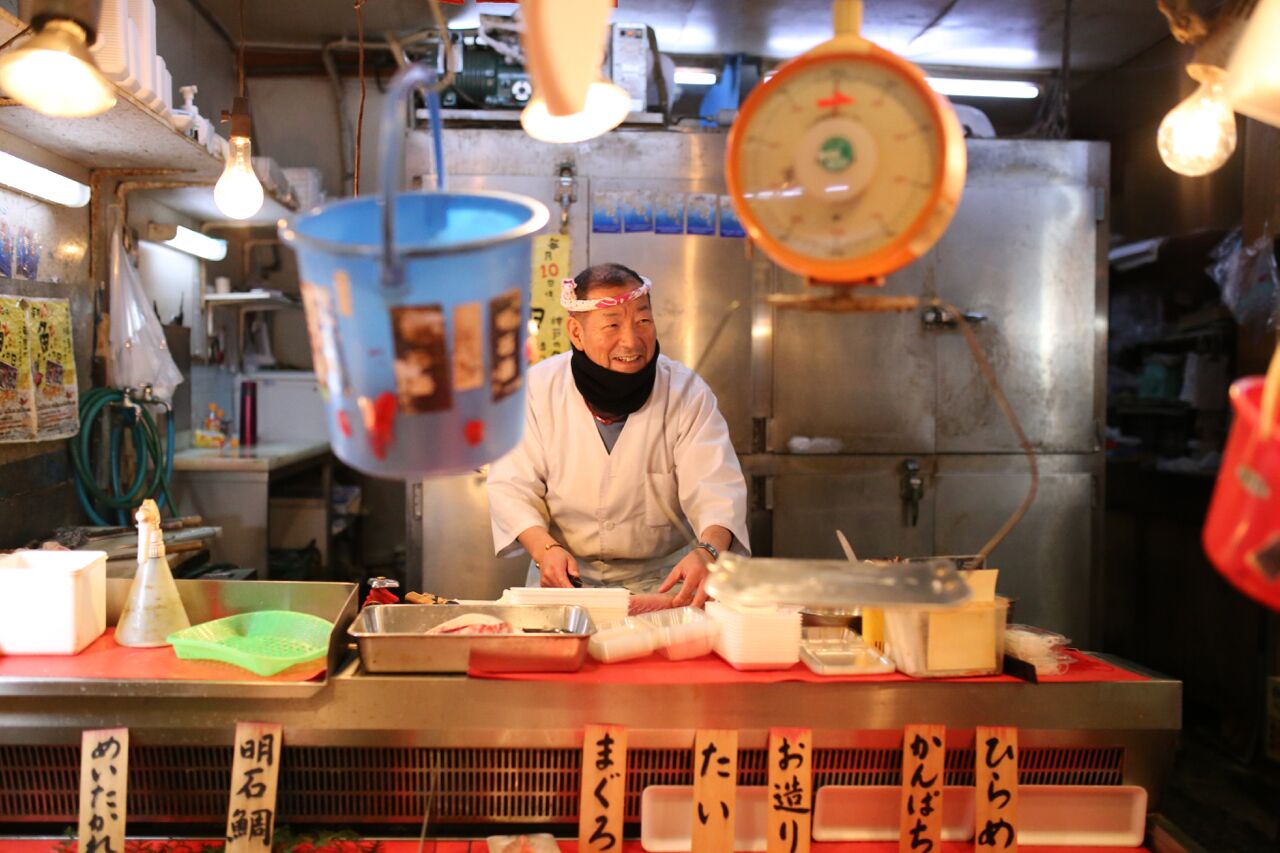 Een kok in een keuken met roestvrijstalen apparatuur en diverse kookgerei en ingrediënten op het aanrecht.