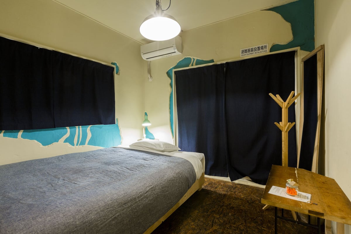 A room with a bed, a small table with a lamp, and a sign on the wall.