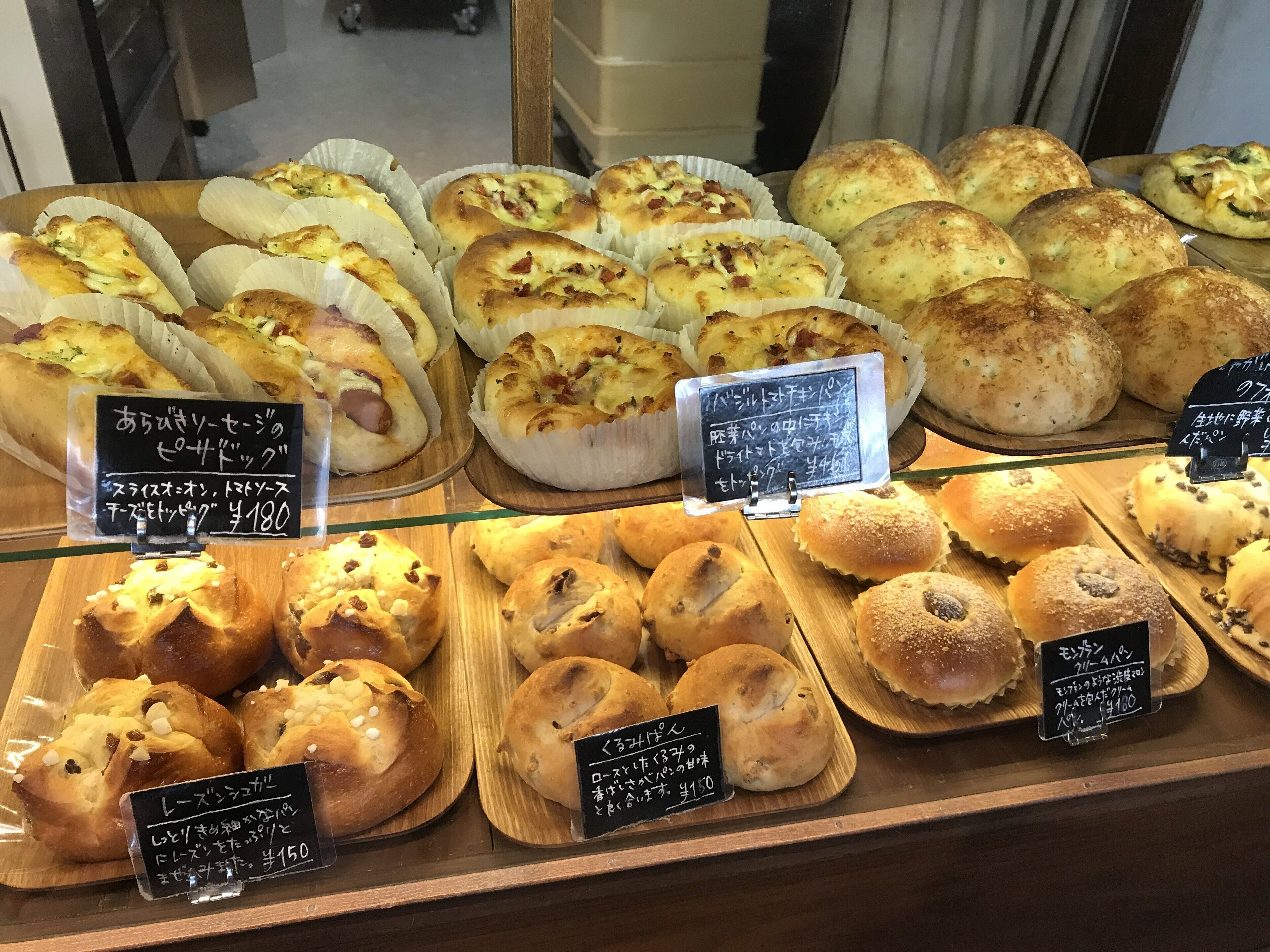 A bakery display with various baked goods, including bread and pastries, with price tags in Japanese.