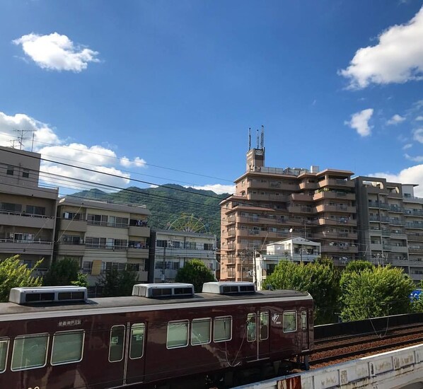 Un tren color burdeos sobre rieles, con montañas y edificios de varios pisos al fondo.
