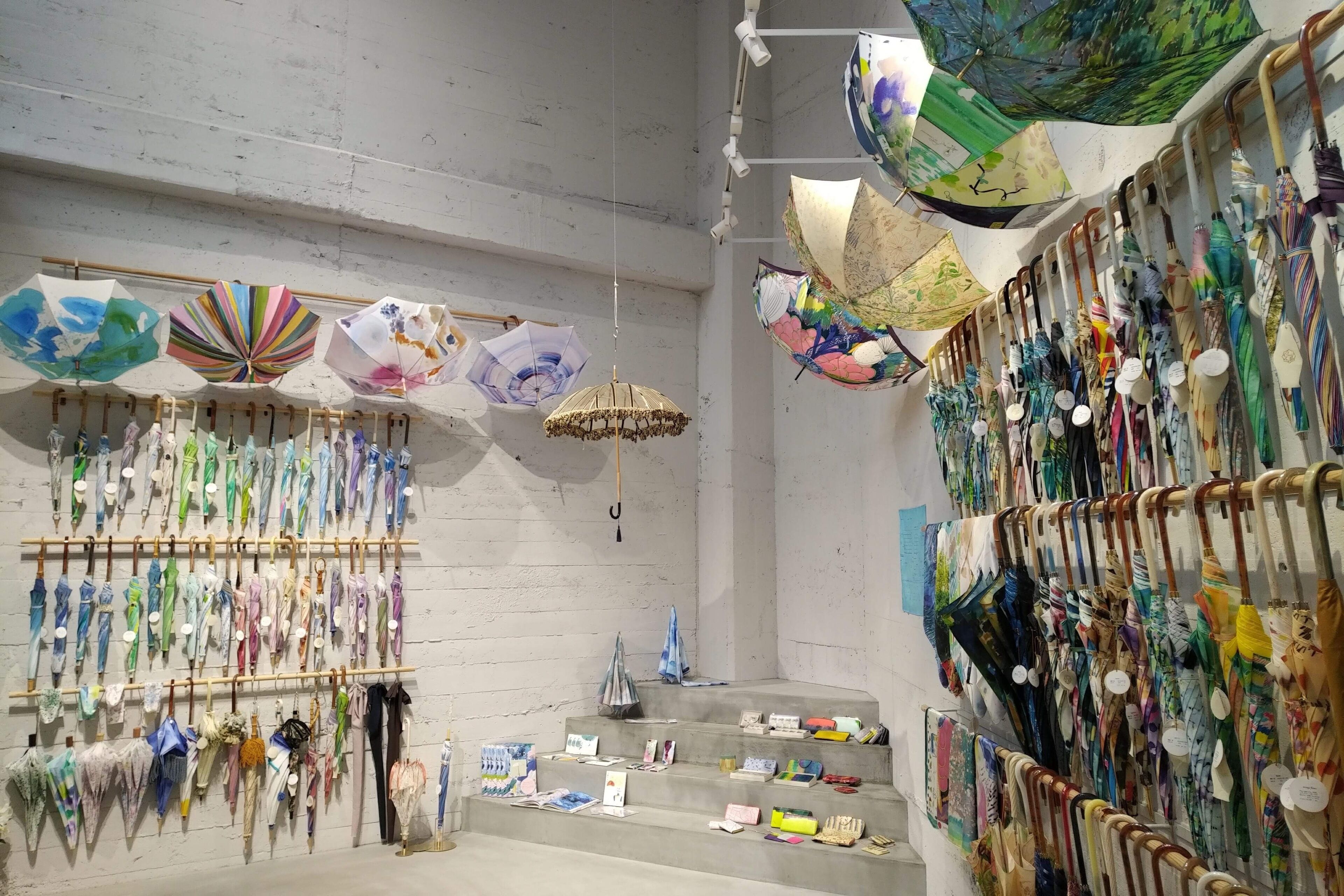 A room with multiple hanging umbrellas and a variety of items displayed on shelves and tables.