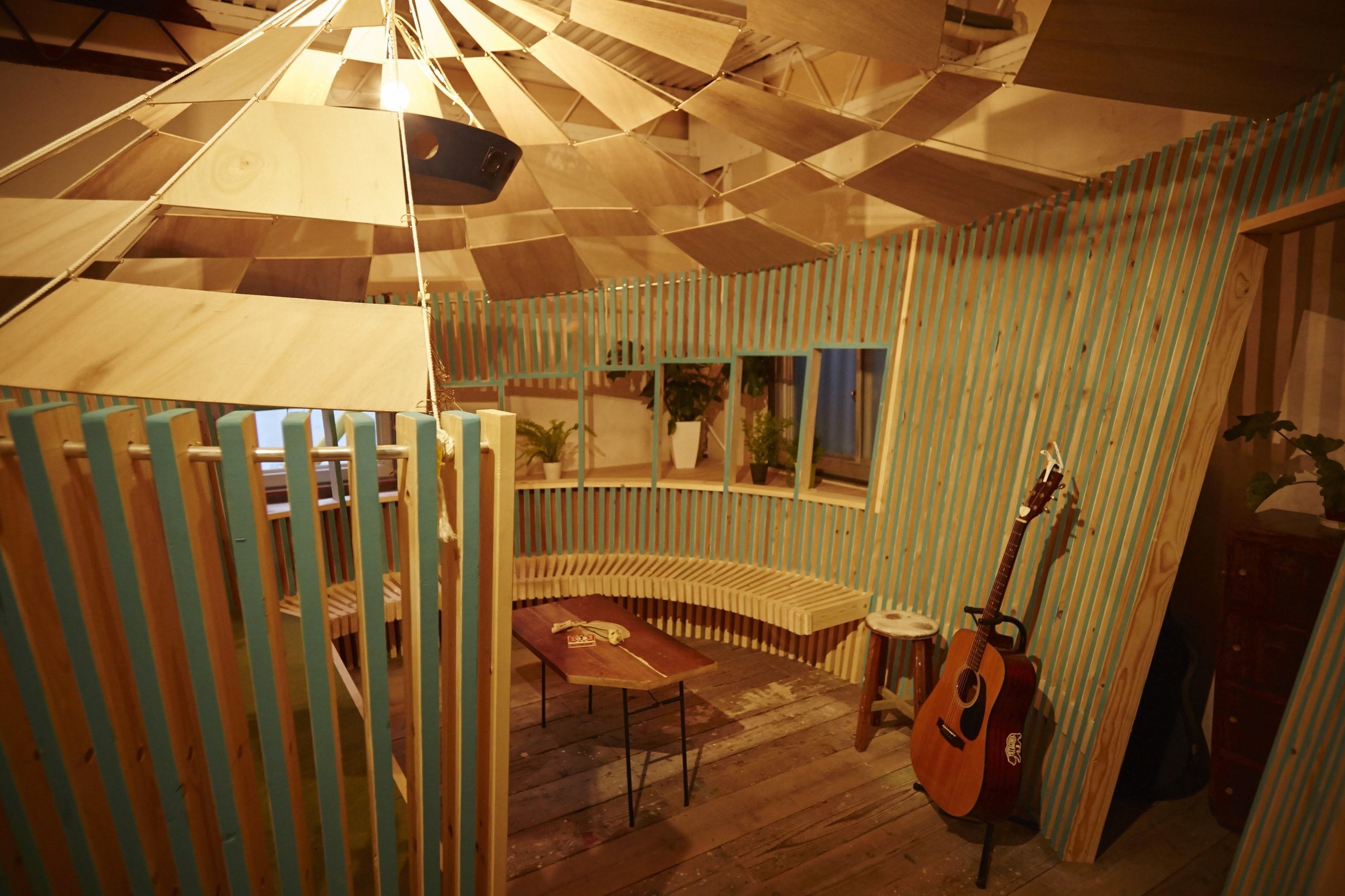 A room with a wooden ceiling, a guitar, a table, and a bench.