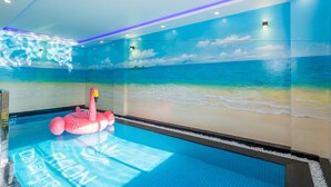 Une piscine ornée d’une fresque représentant une plage, un flotteur en forme de flamant rose et un éclairage à DEL.