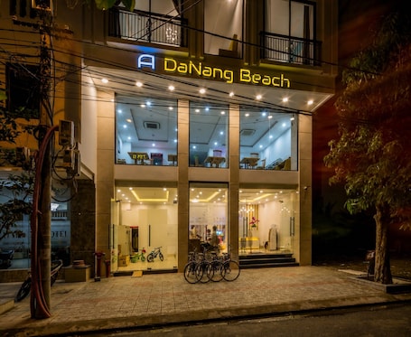 A hotel named Da Nang Beach with a modern facade, large windows, and a bicycle parked outside.