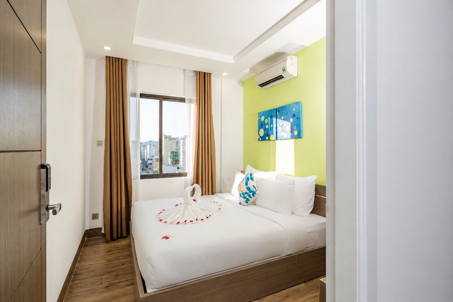 A hotel room with a bed, a window, curtains, an air conditioning unit, and a city view.