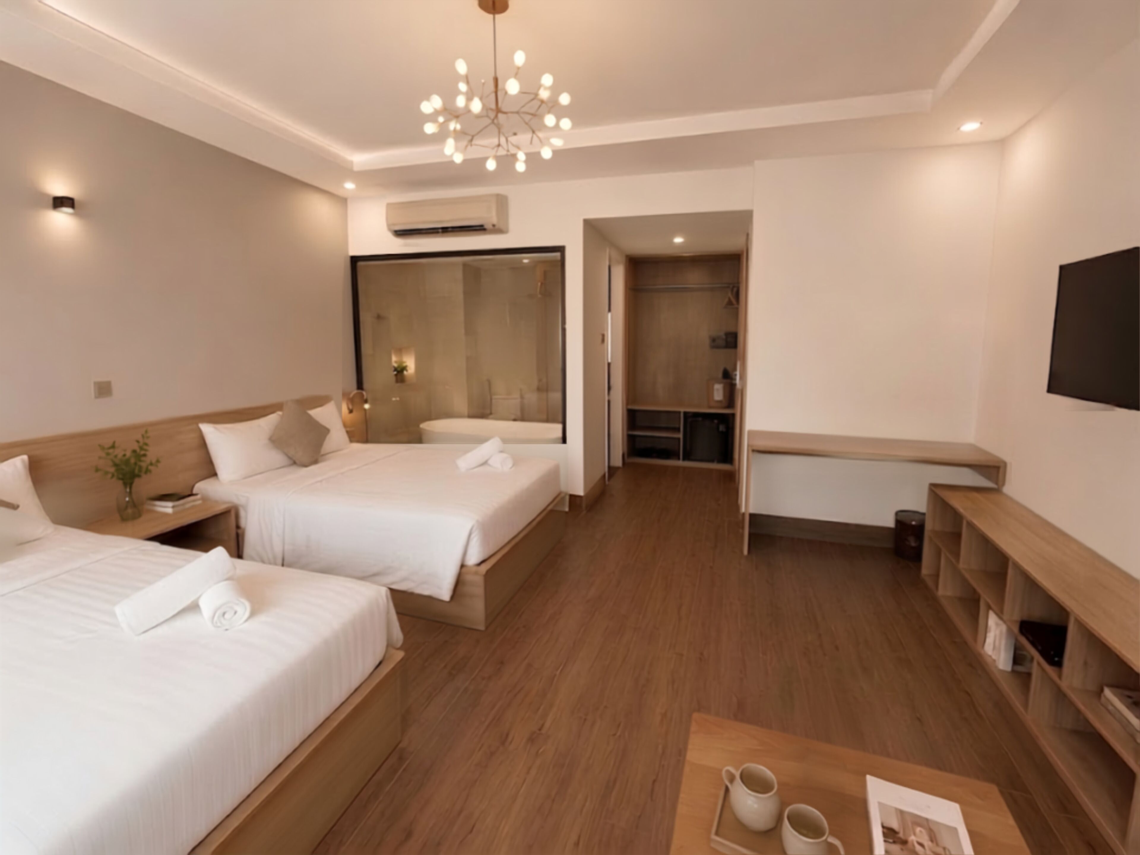 A hotel room with two beds, a sitting area with a coffee table, a TV, and a bathroom with a bathtub.