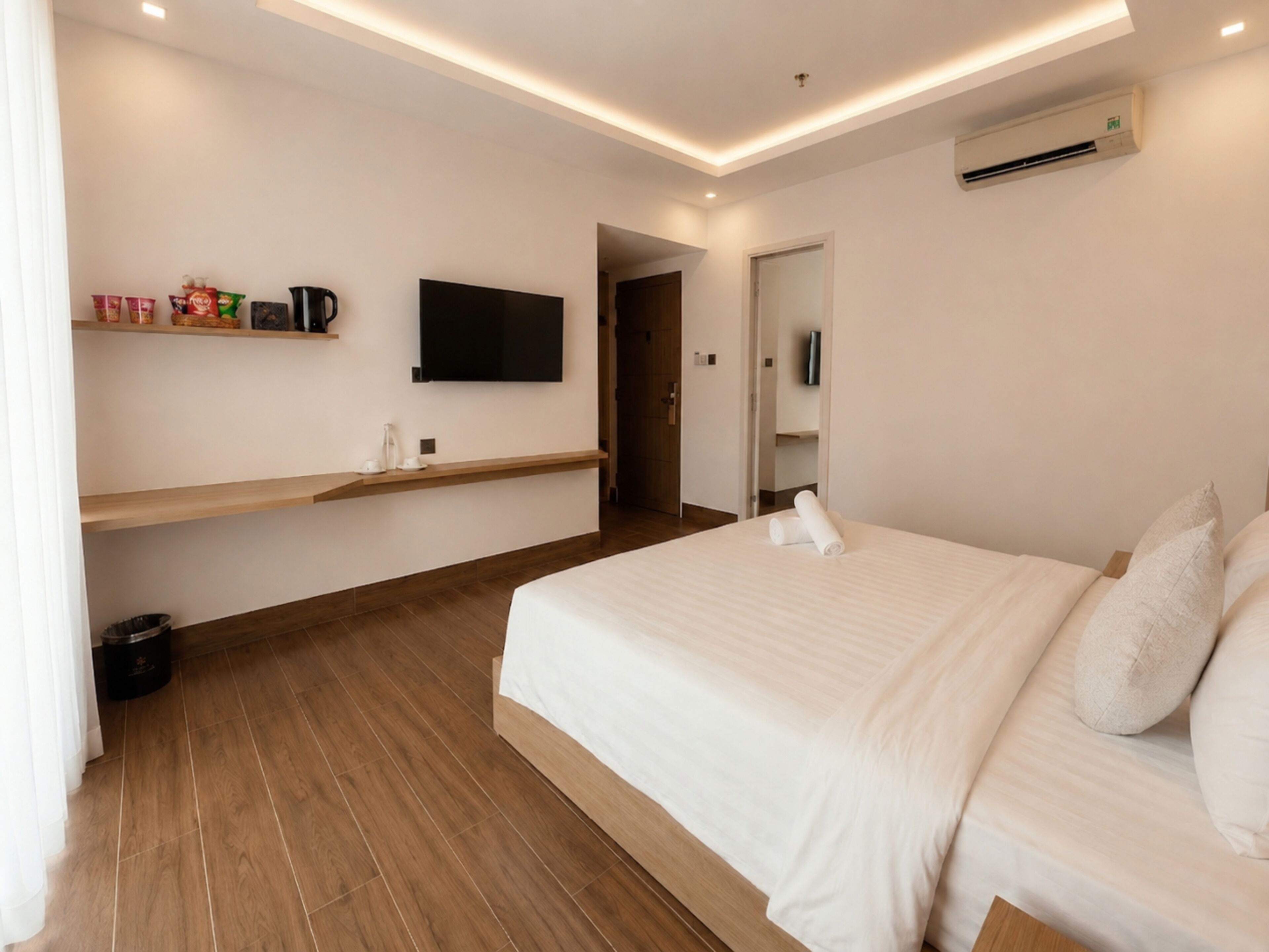 Une chambre d’hôtel moderne dotée d’un grand lit, d’un téléviseur à écran plat fixé au mur, d’un plancher en bois et d’une étagère intégrée où sont rangés les articles de toilette.
