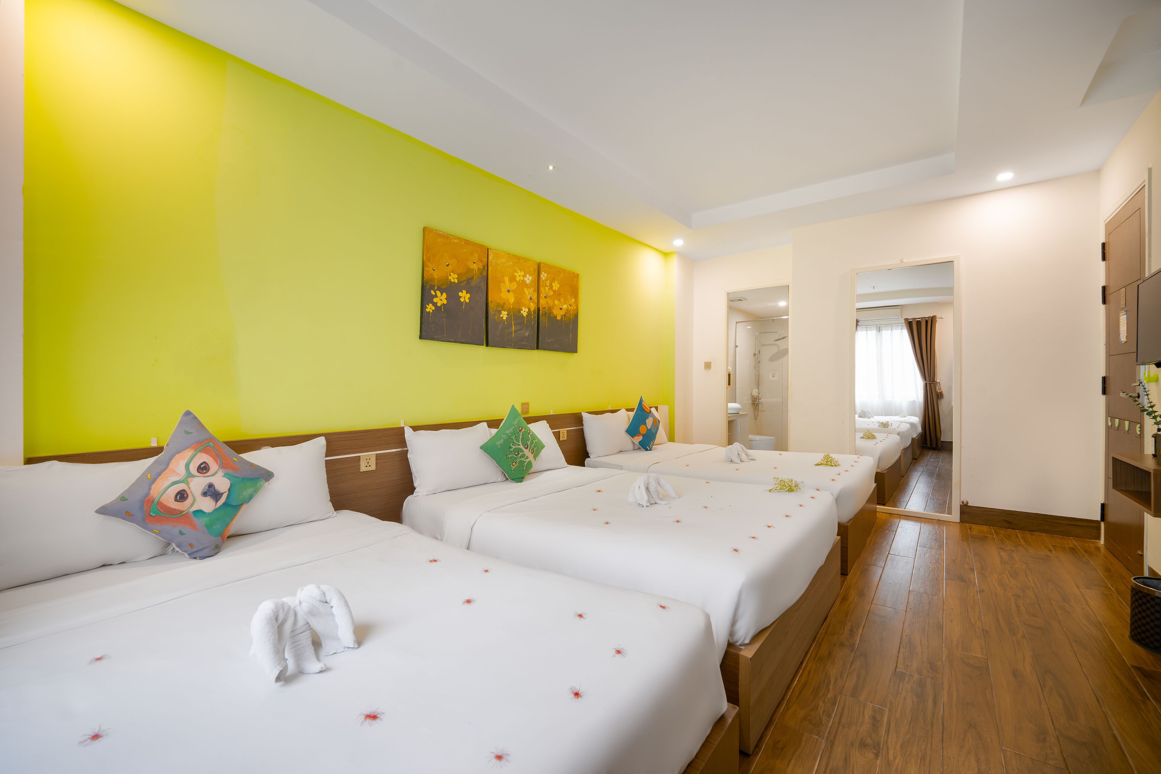 Une chambre d’hôtel avec trois lits, un mur jaune vif et un plancher en bois.