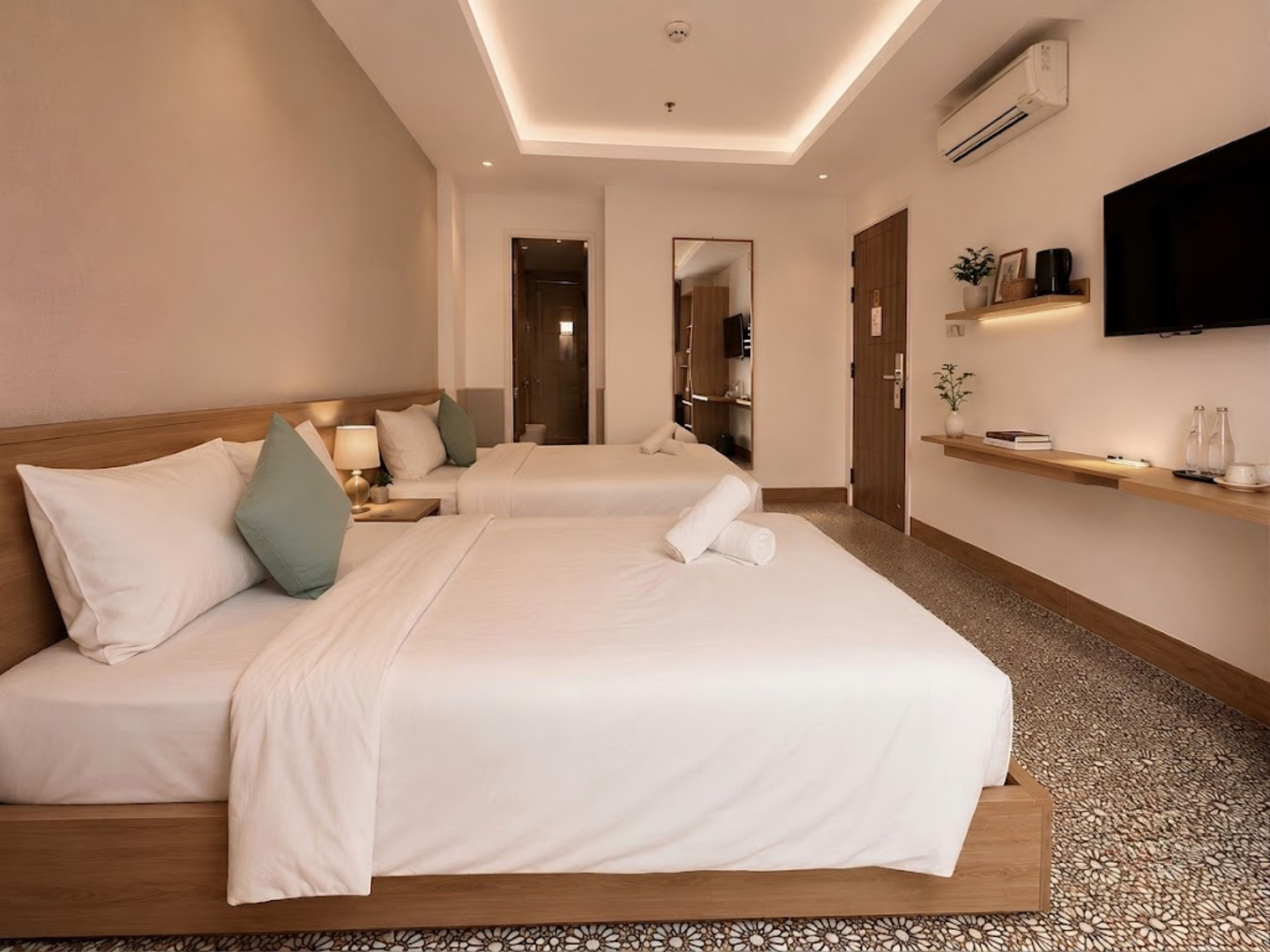 Une chambre d’hôtel avec deux lits, une télévision, une étagère avec quelques objets et un miroir.
