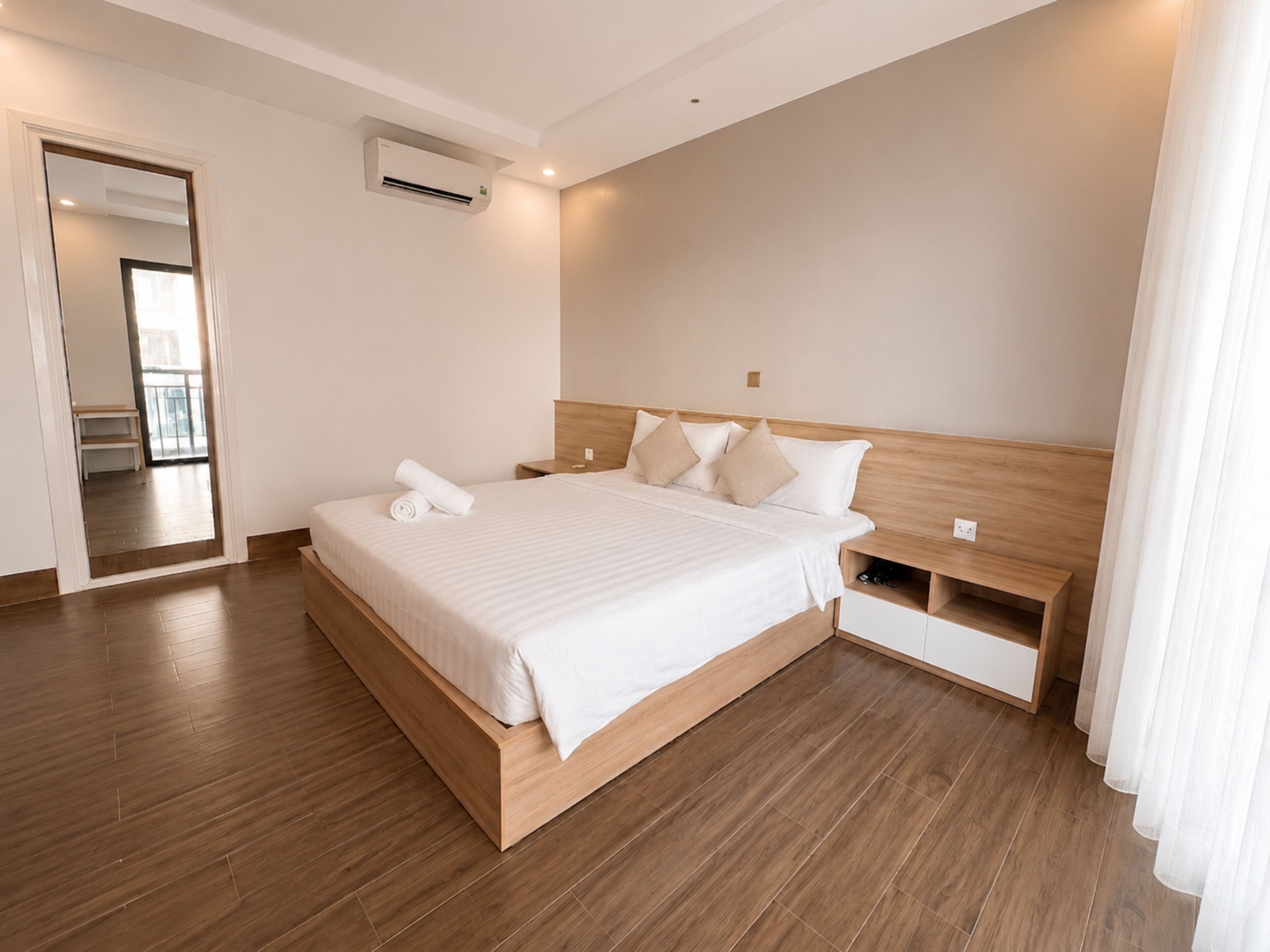 Una habitación de hotel moderna con una cama de madera, una mesita de noche, un estante empotrado y un espejo grande.