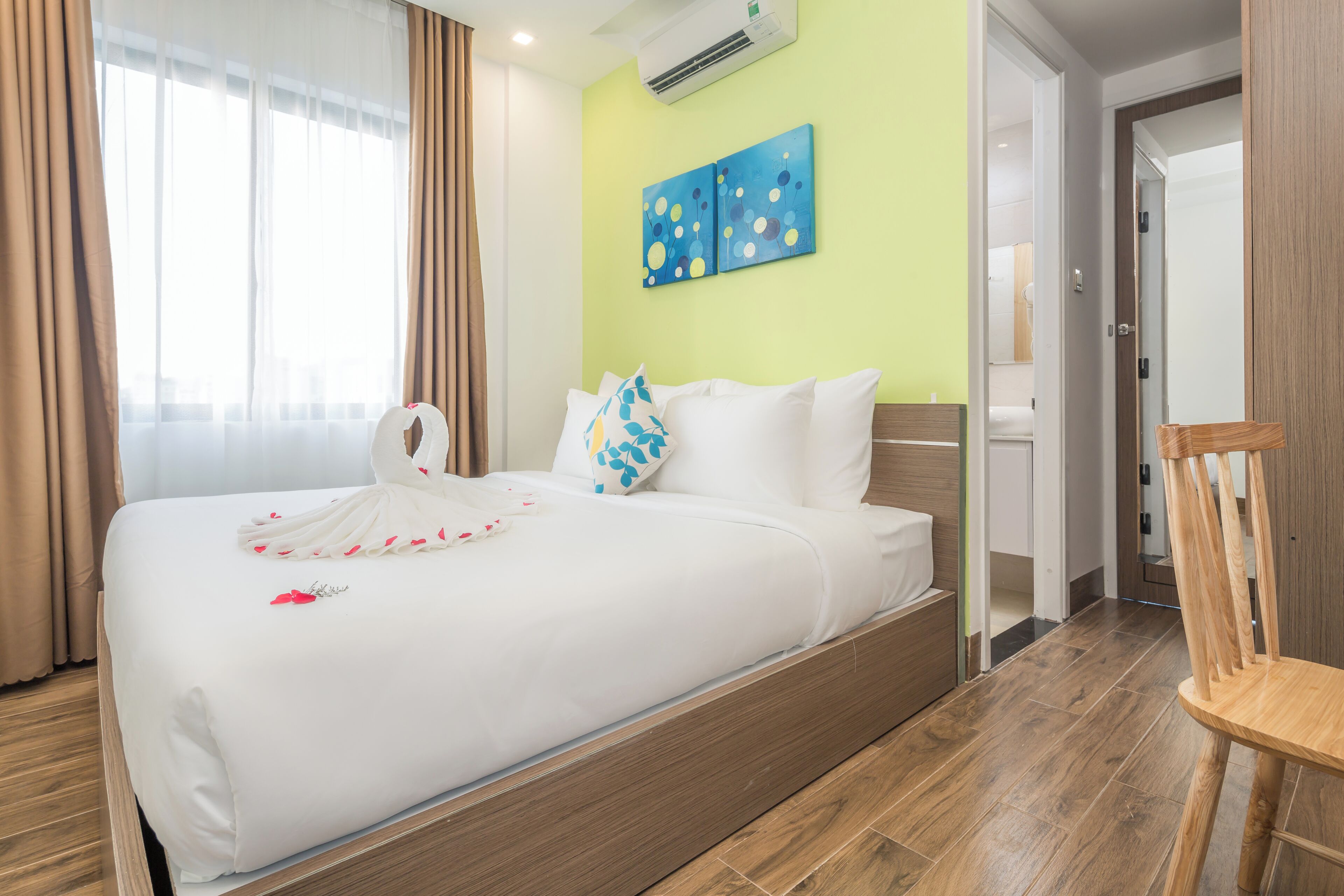 A hotel room with a large bed, a wooden chair, a green wall, and a painting.