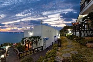 Un hotel moderno con fachada blanca, terraza de madera y vista al mar al atardecer.