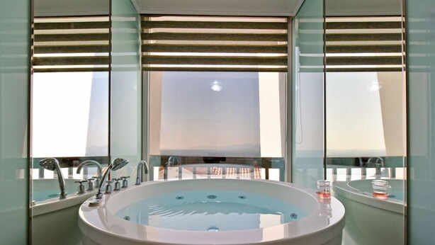 Un baño moderno con una bañera independiente grande, una zona de ducha con mampara de vidrio y vistas a la silueta urbana a través de amplias ventanas.
