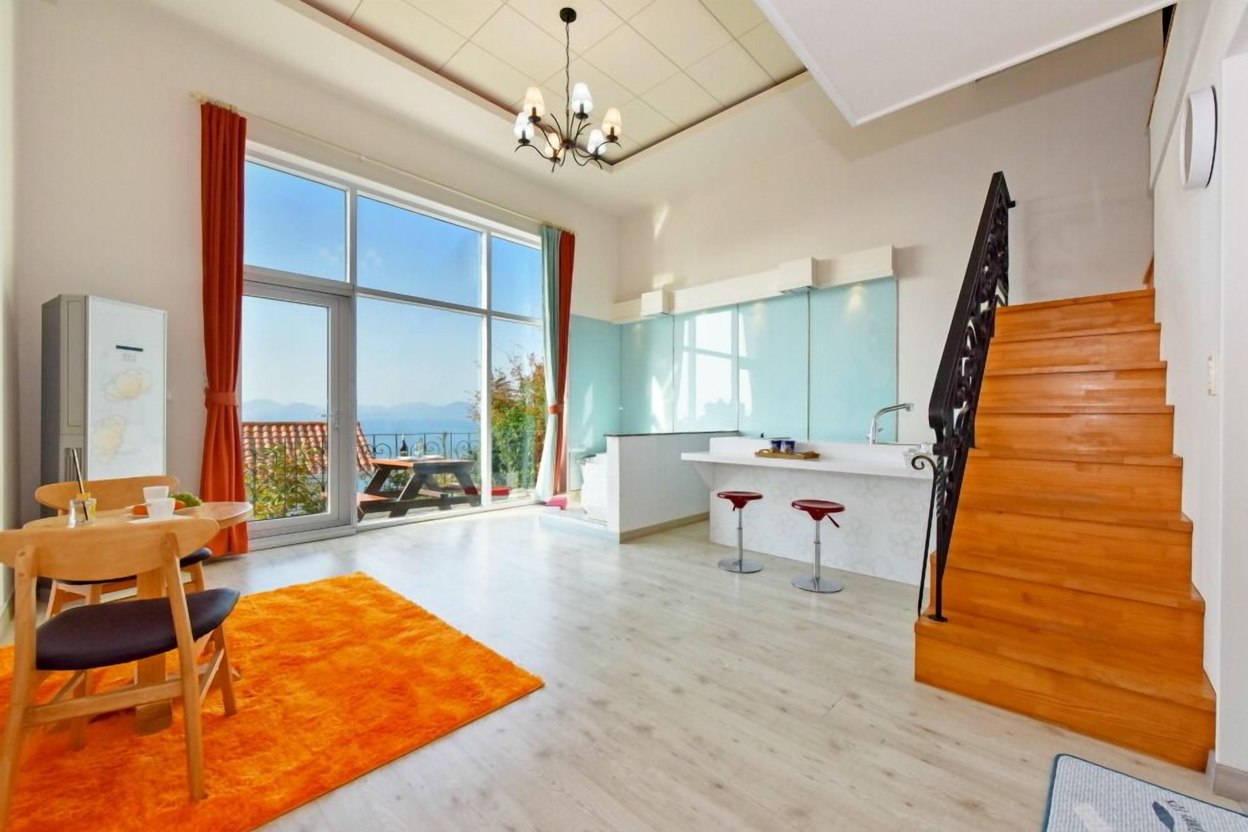 Un apartamento moderno con un gran ventanal corredero que da a un balcón, una zona de cocina con barra y una escalera.