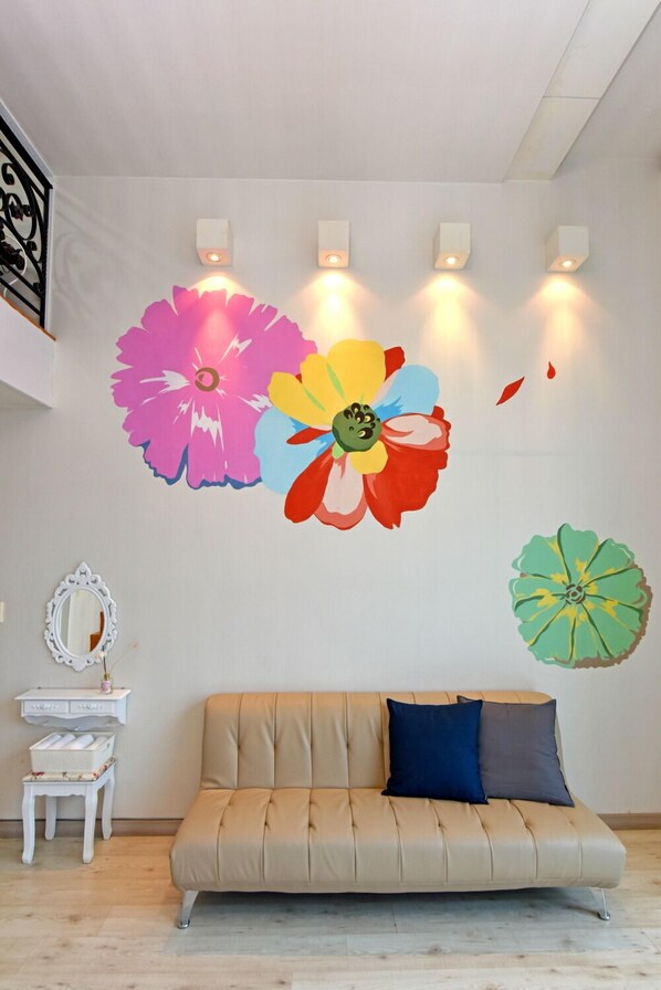 A room with a beige sofa, a white side table with a mirror, and a wall with colorful flower murals.