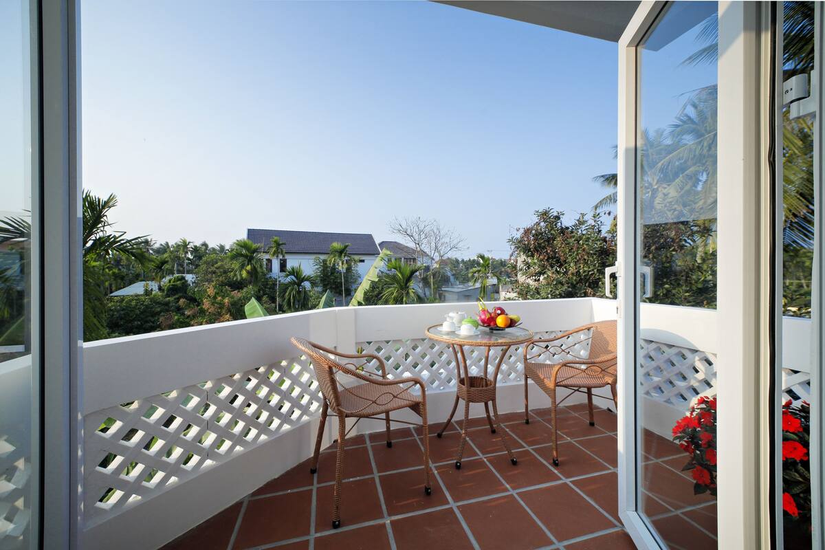 A balcony with wicker furniture, a table with a fruit bowl, and a view of palm trees and buildings.