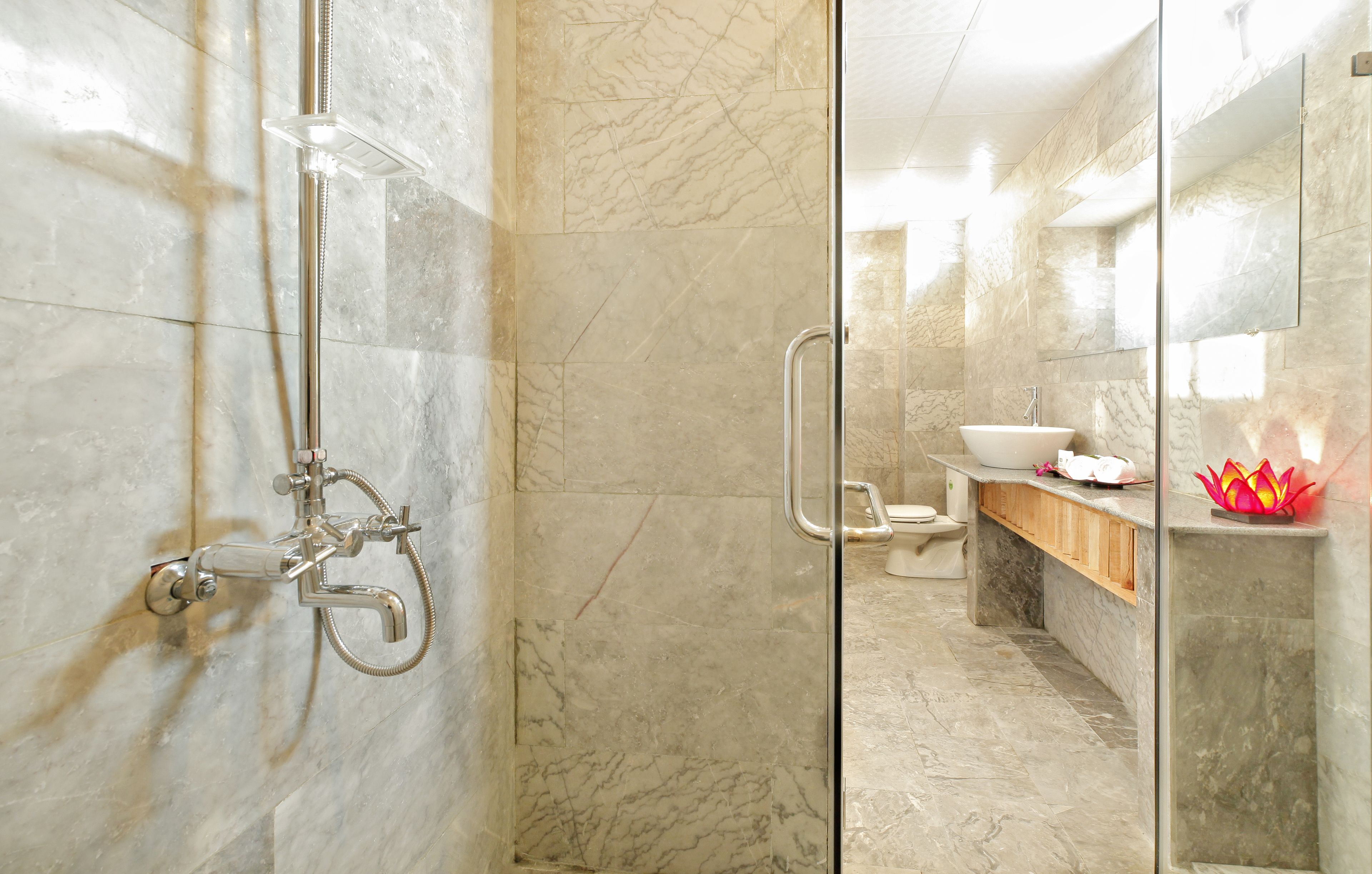 A modern bathroom with a glass-enclosed shower, a marble-tiled floor, a wooden vanity, and a large mirror.