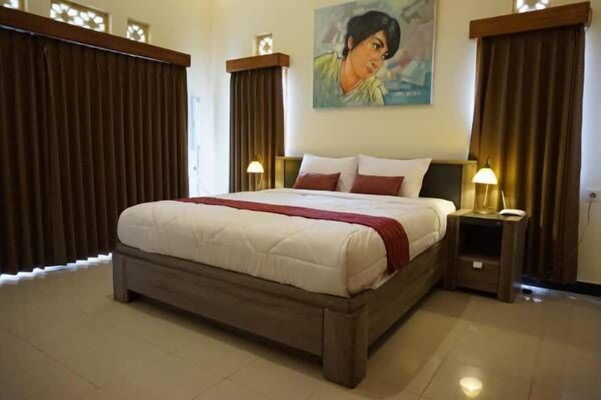 Una cama grande con cabecera de madera, dos mesitas de noche con lámparas, y un cuadro en la pared.