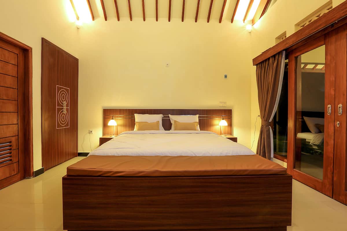 Un dormitorio bien iluminado con una cama grande, cabecera de madera y puerta corrediza de vidrio que da a un balcón.