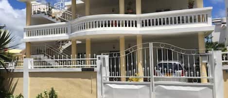 A two-story building with a white exterior, a gated entrance, and a staircase leading to the upper floor.