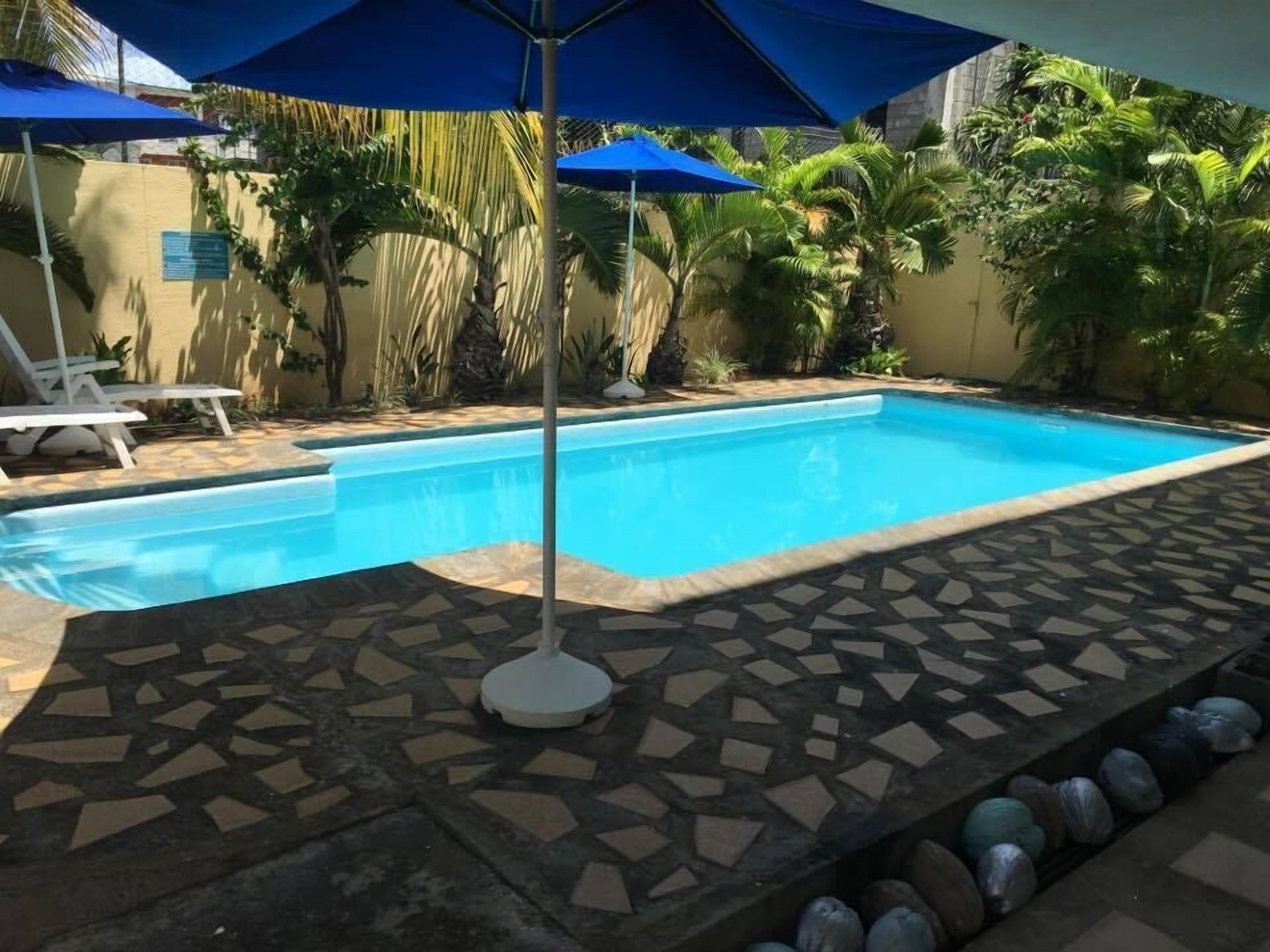 A swimming pool with a tiled deck, surrounded by palm trees and blue umbrellas.