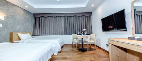 Una habitación de hotel con dos camas, una mesa de comedor con sillas, un televisor y un escritorio de madera.