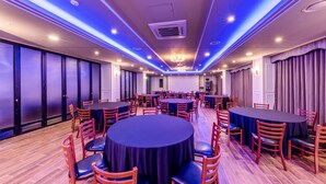 Une salle de conférence dotée de tables et de chaises rondes, équipée de luminaires encastrés au plafond et d’un lustre.