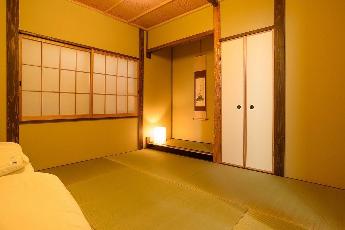 A traditional Japanese room with tatami flooring, sliding doors, and a bed with a white comforter.
