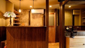 A wooden reception desk with a stained glass lamp, a wall-mounted air conditioner, and a wooden floor. - Guesthouse Gokurakudo - Hostel (Kyoto)