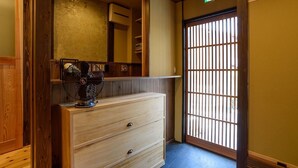 A traditional Japanese room with a wooden dresser, a fan, and a sliding door with vertical bars. - Guesthouse Gokurakudo - Hostel (Kyoto)