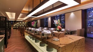 A buffet setup with multiple food stations, a marble counter, and a view of a forest through a large window. - Relaxed Season Hotel - Foshan (Foshan)