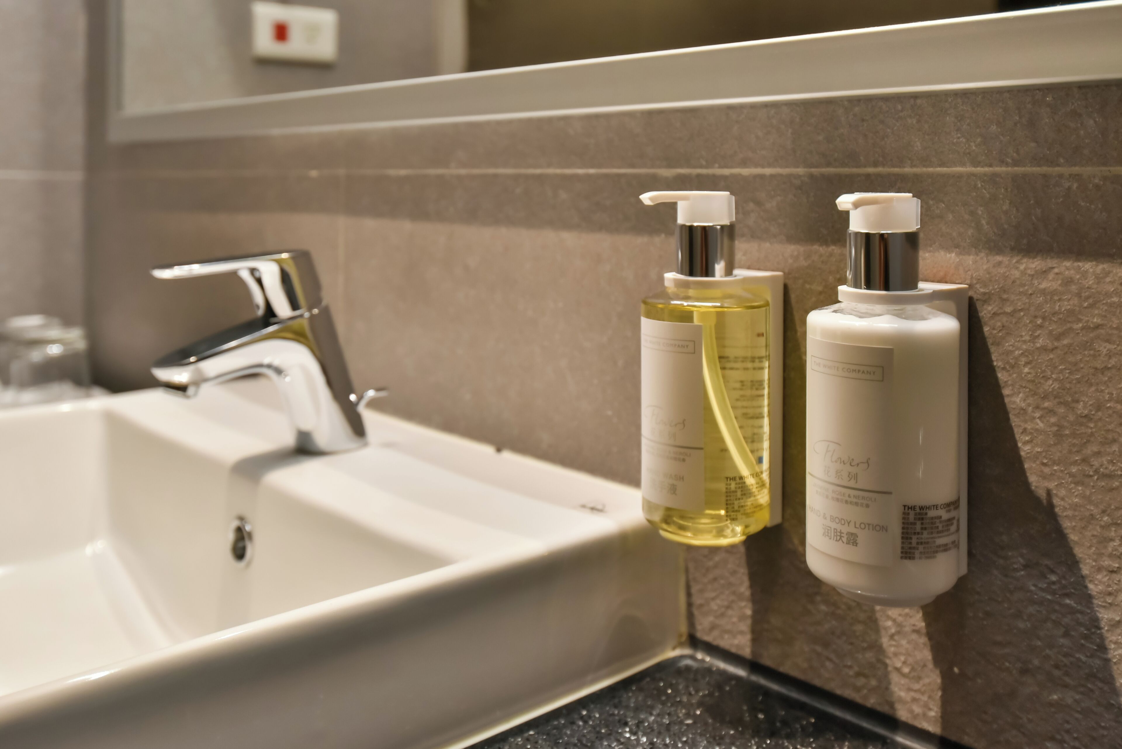 A bathroom sink with a chrome faucet and two bottles of lotion on the wall.