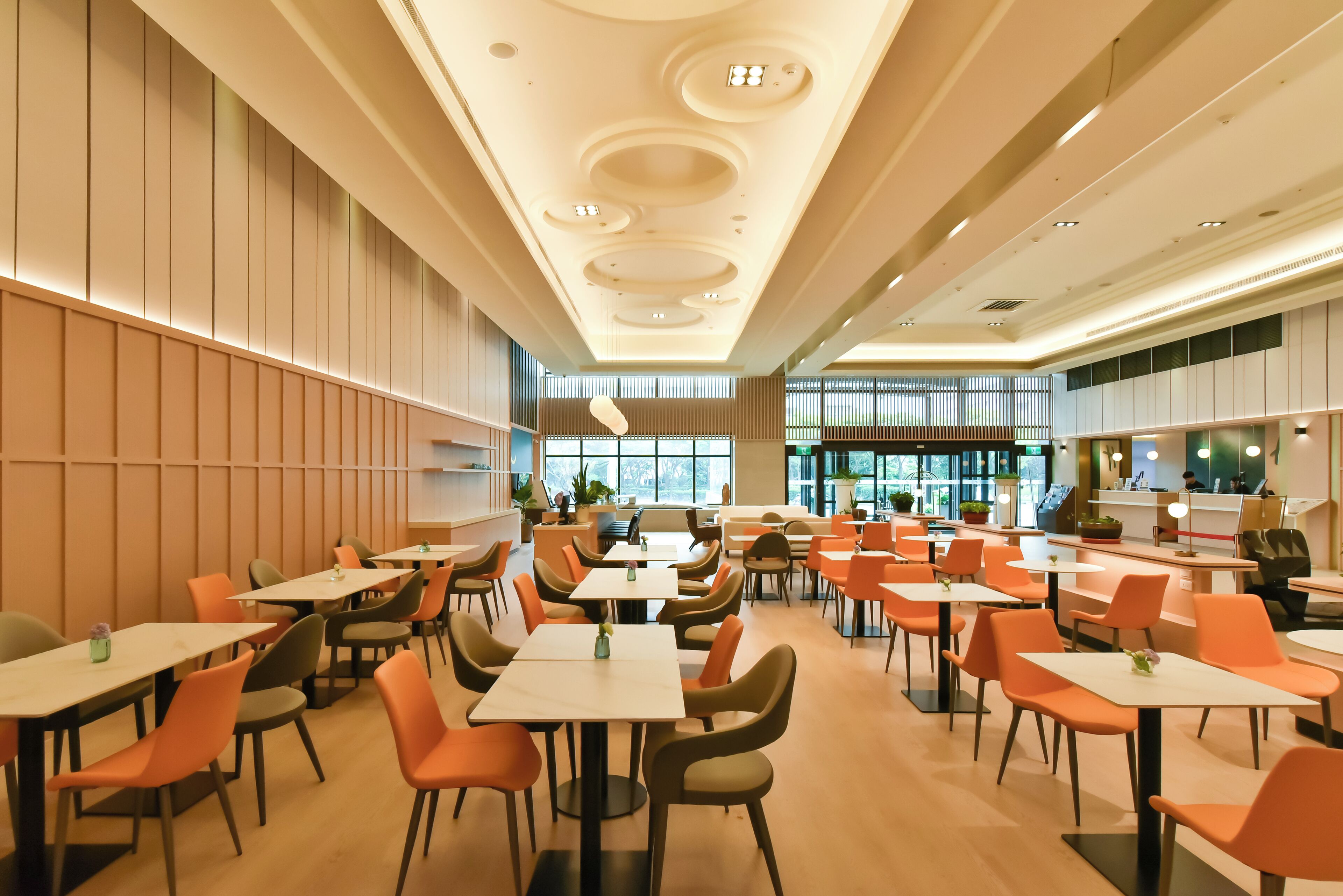 Un restaurante espacioso con numerosas mesas y sillas, un diseño de techo moderno y grandes ventanales que permiten la entrada de luz natural.