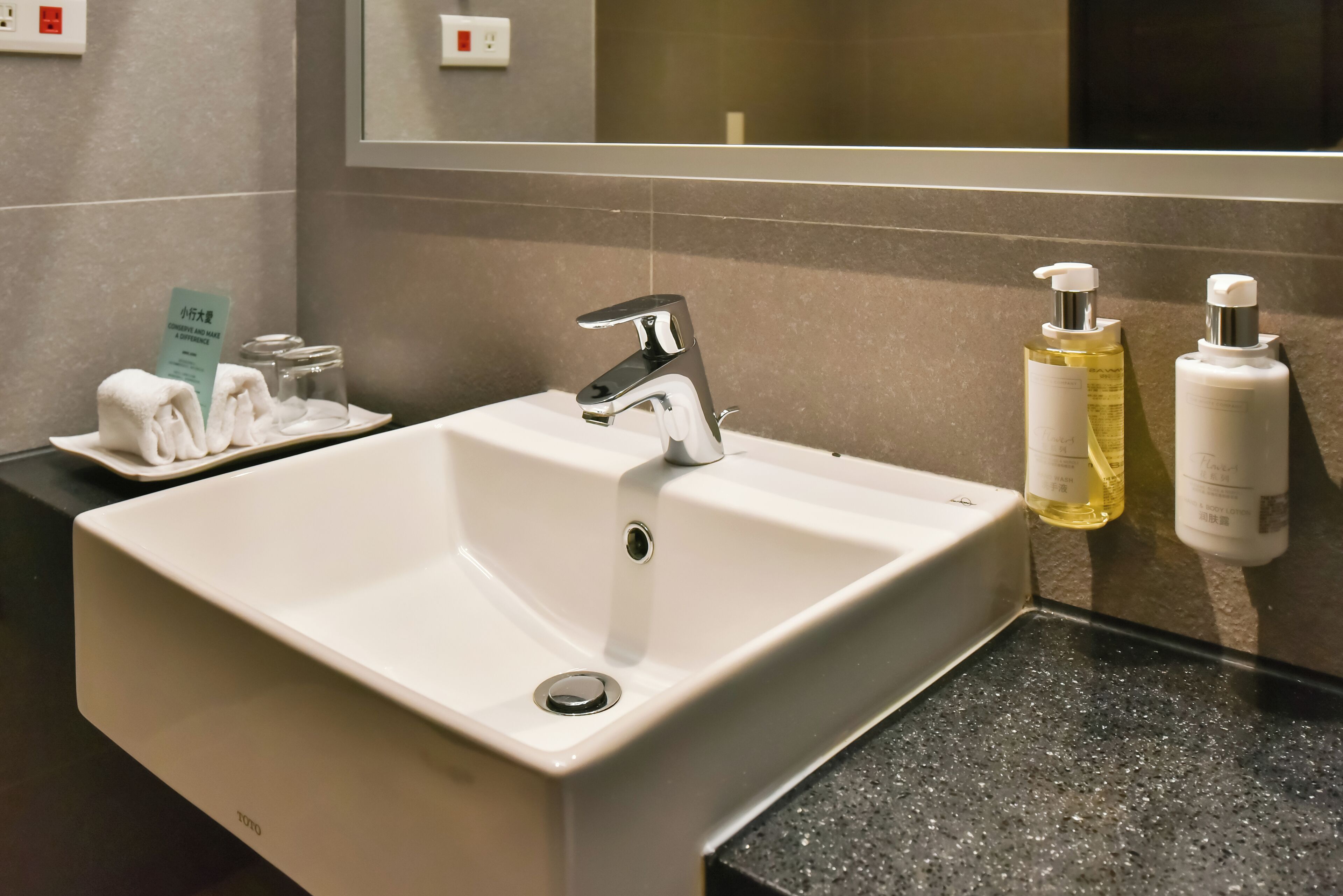 A hotel bathroom with a white sink, a mirror, and toiletries on the wall.