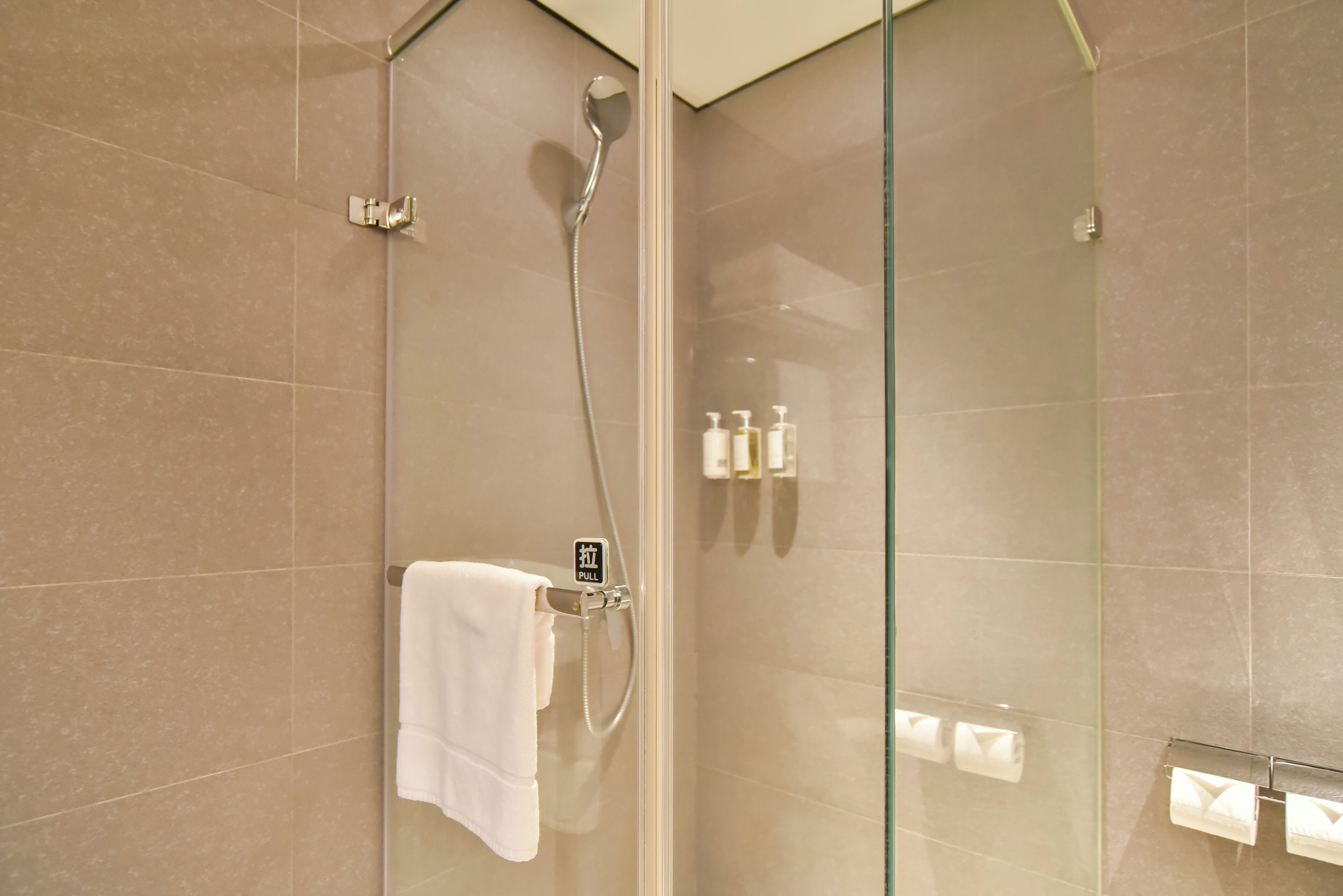 A glass-enclosed shower area with a towel rack and toiletries.
