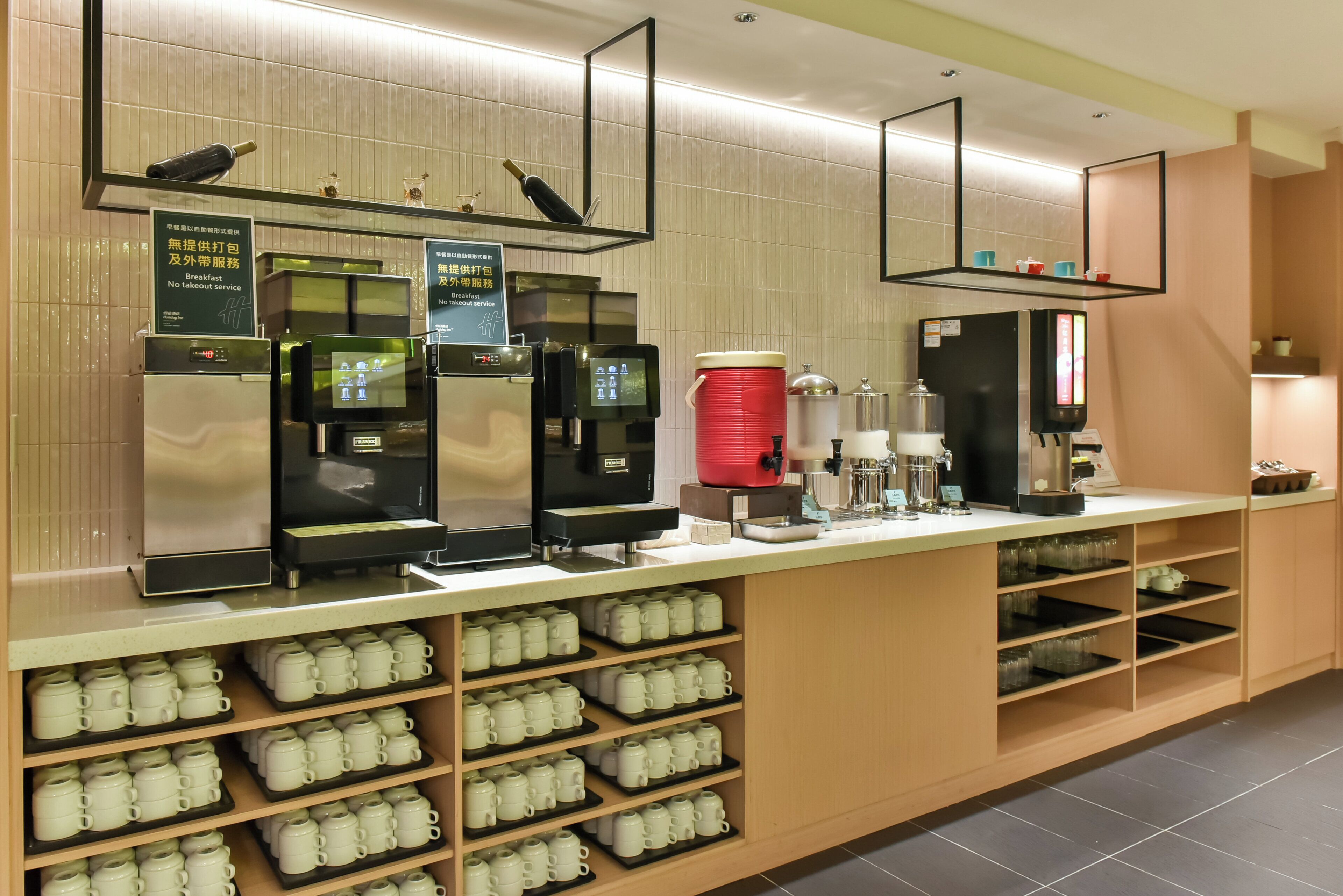 Una estación de café autoservicio con varias máquinas de café, un dispensador de café rojo y una variedad de tazas y vasos en estantes.