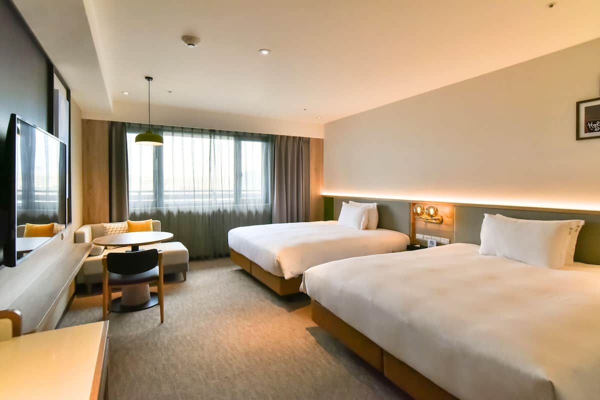 A hotel room with two beds, a desk, a chair, and a window with curtains.