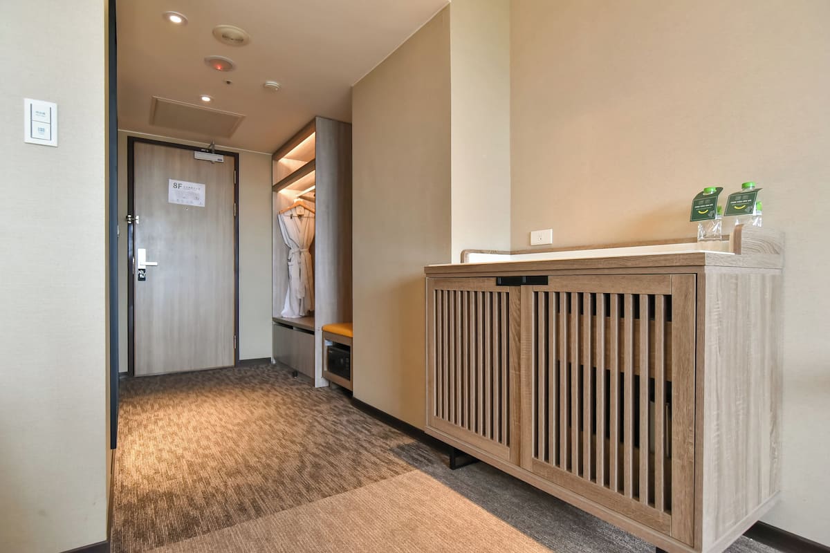 Un couloir d’hôtel avec un banc en bois, un porte-manteau et un meuble sur lequel sont posées des bouteilles vertes.
