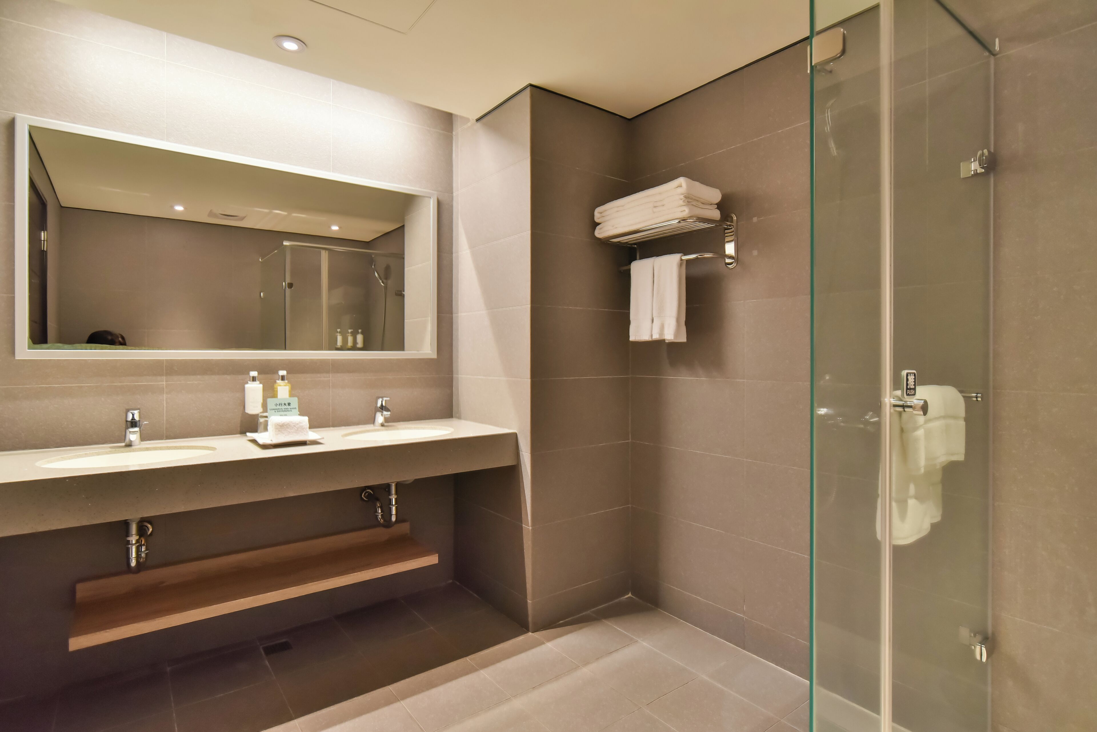 Een moderne badkamer met een douche met glazen wand, een grote spiegel en een wastafel met twee kommen.