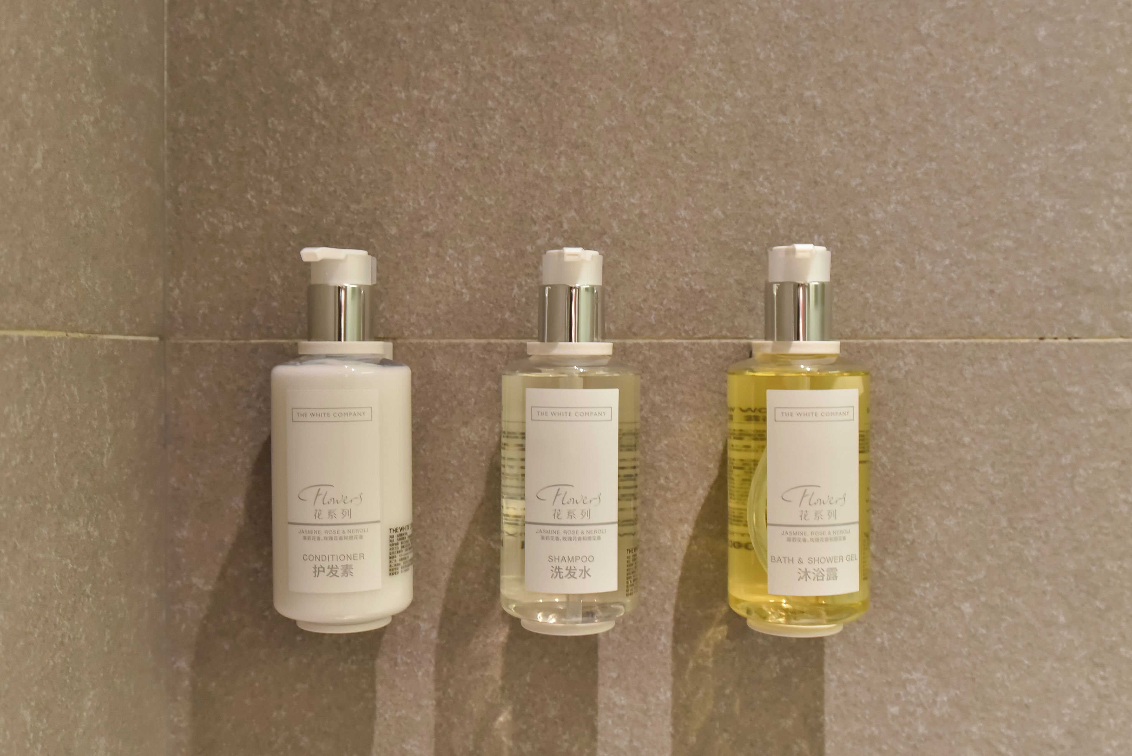 Tres botellas de productos de The White Company sobre un muro de azulejos.