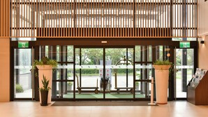 Entrada de un hotel de diseño moderno, con puerta de vidrio con marco metálico, dos plantas en macetas y un mostrador de recepción a la derecha.